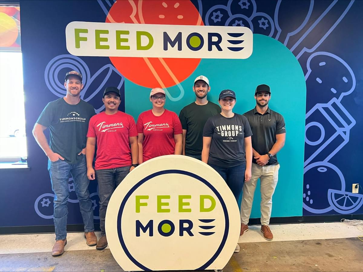 Timmons Group land development team members pose standing in front of a "Feed More" sign for a photo.