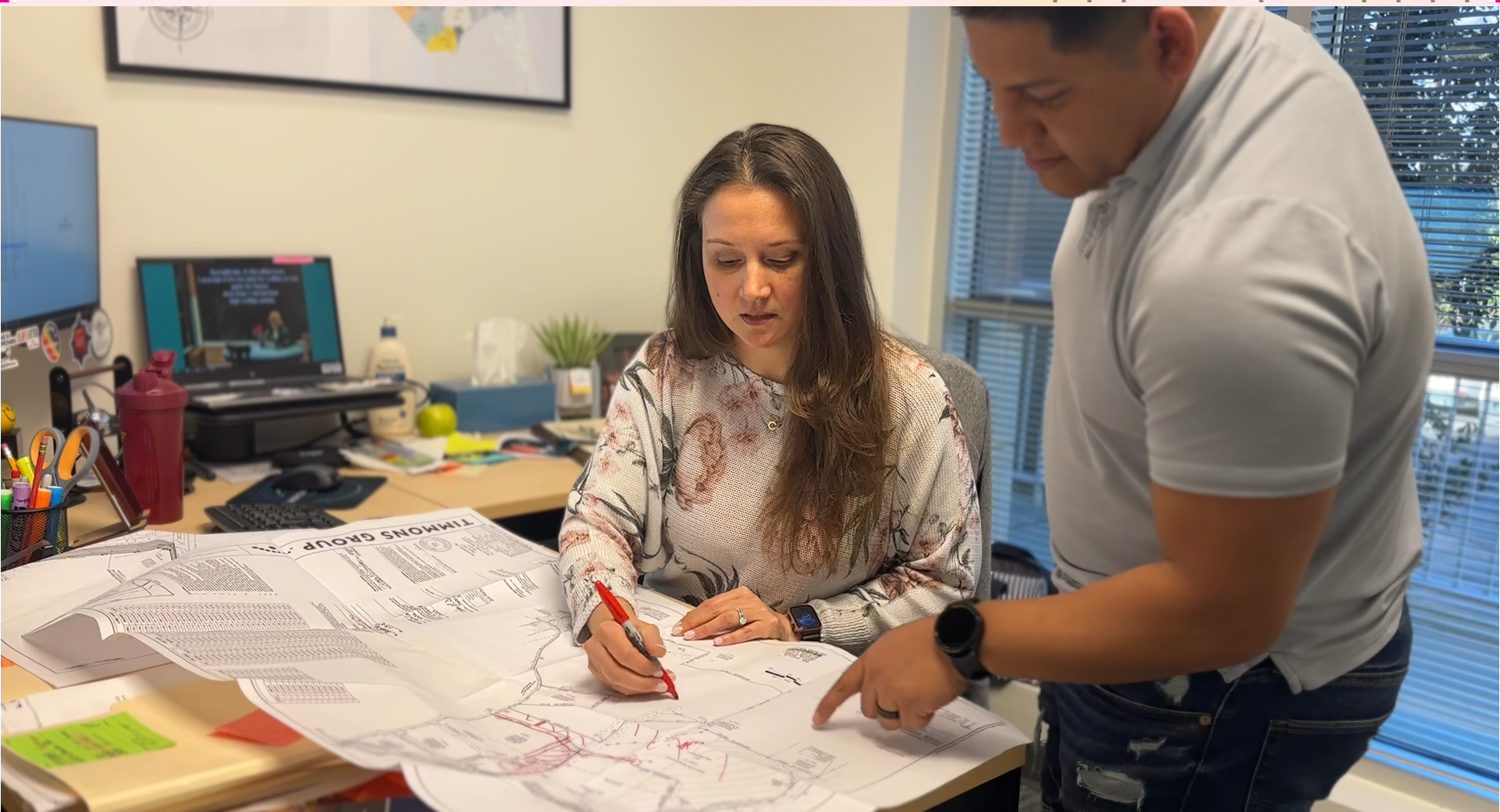 Alicia mentoring another employee by making corrections on a paper plan with a red sharpie.