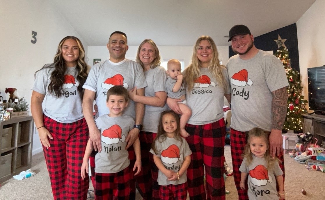 Sunni and her family wearing matching Christmas pajamas that include red and black plaid pants and gray t-shirts with red and white santa hats in the middle and their names underneath.