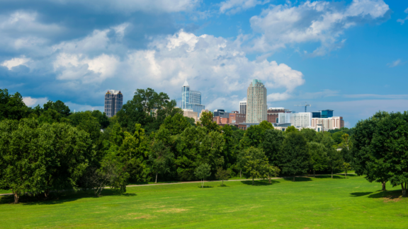 A picture of an open field at Dix Park with the skyline of the City of Raleigh in the background