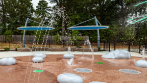 A water play area in the shape of rocks in dirt at the Beluah Park playground, the rocks are squirting water.