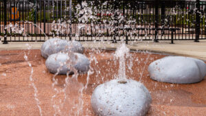 A water play area in the shape of rocks in dirt at the Beluah Park playground, the rocks are squirting water.