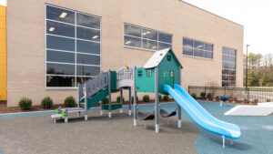 A piece of playground equipment with a house-shaped hut and a slide out with the Southside Community Center in the background.
