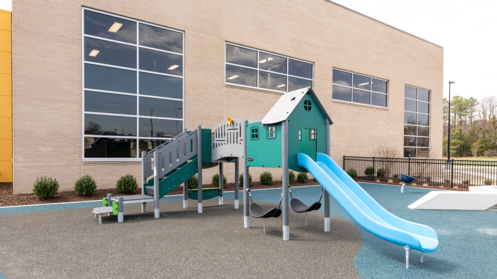 A piece of playground equipment with a house-shaped hut and a slide out with the Southside Community Center in the background.